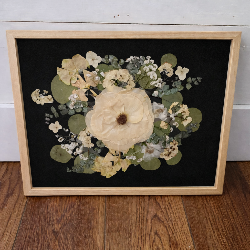 Framed pressed flowers in a natural wood frame on a black background with a wooden frame.