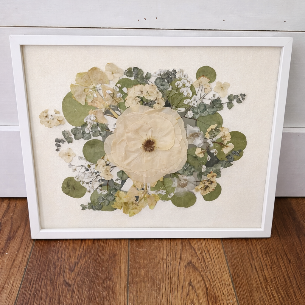 White framed artwork with pressed flowers on an ivory mat on a wooden floor